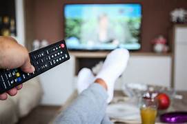 A person in gray sweatpants and white socks holds a remote control while watching television, showcasing a cozy indoor setting.